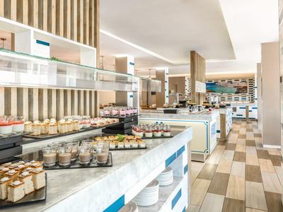 Sala da pranzo di un hotel luminosa con design moderno e buffet di dessert e bicchieri.