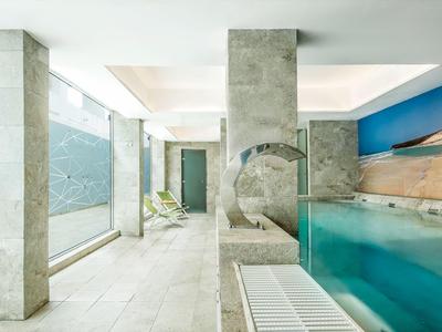 Piscina interna luminosa e moderna con grandi finestre e rivestimento in pietra naturale.