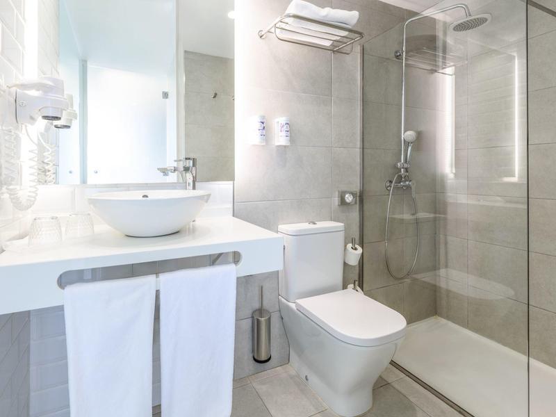 Bagno luminoso con lavabo, toilette e doccia a filo con piastrelle grigio chiaro.