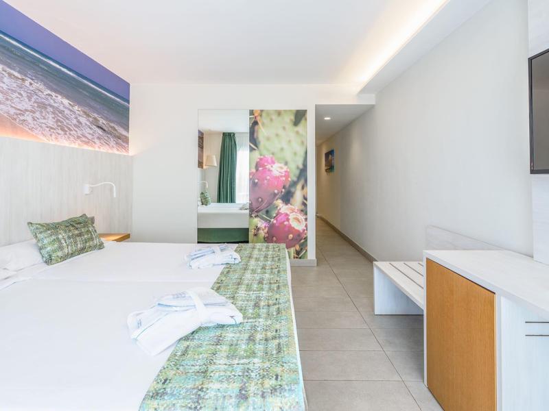 Camera d'hotel moderna con letto matrimoniale, cuscini verdi a motivi e grande quadro murale della spiaggia.