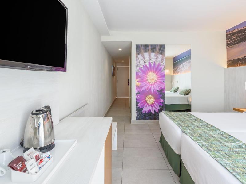 Camera d'hotel moderna con TV, bollitore, letto matrimoniale e porta floreale colorata.