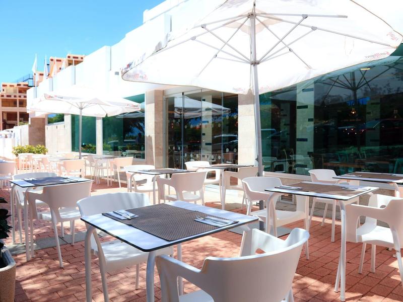 Terrazza esterna luminosa dell'hotel con tavoli, sedie e ombrelloni bianchi.