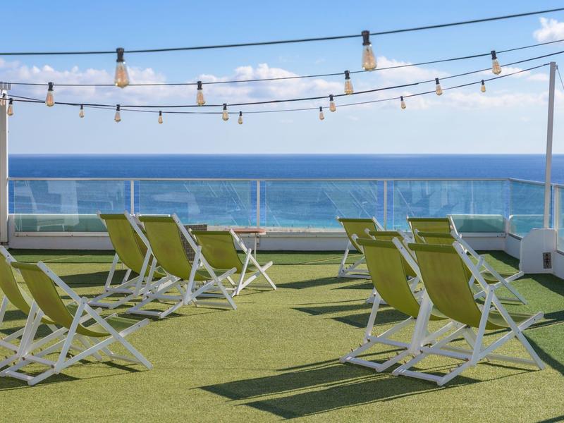 Terrazza sul tetto con sedie a sdraio con vista sul mare sotto un cielo azzurro.