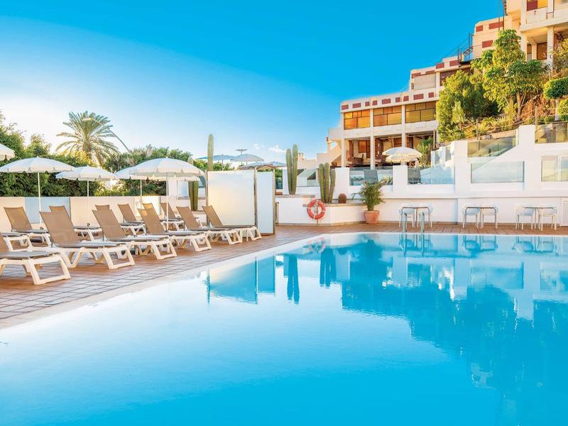 Piscina esterna limpida con lettini e ombrelloni davanti a un edificio dell'hotel.