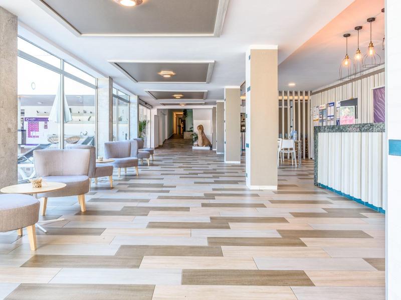 Corridoio d'hotel luminoso con grandi finestre, aree salotto e design moderno.