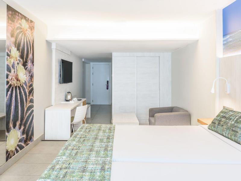 Camera d'hotel luminosa con letto matrimoniale, scrivania, divano e arredamento moderno.