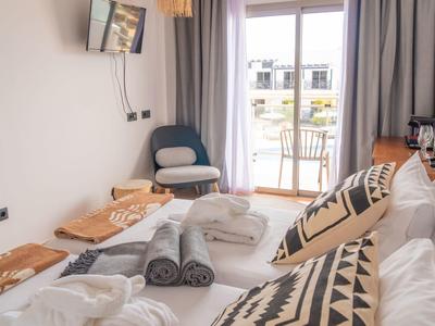 Helles Schlafzimmer mit Bett, Kissen in Schwarz-Weiß, grauen Handtüchern und einem Balkon mit Stühlen.