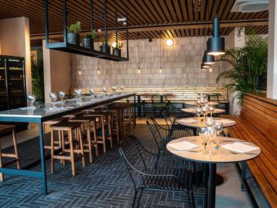 Modernes Restaurant mit Holzdecke, Steinwand, runden Tischen, Stühlen und Bar mit Hockern.