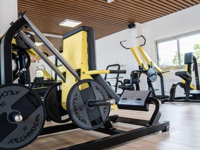 Fitnessraum mit Kraftmaschinen, Fahrradergometern und Holzboden unter hellem Deckenlicht.