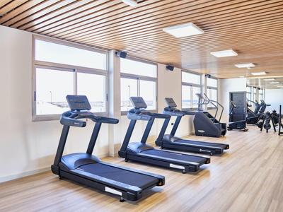 Moderner Fitnessraum mit drei Laufbändern, Holzdecke, großen Fenstern und hellen Holzboden.