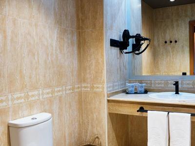 Kleines Badezimmer mit beigem Fliesen, weißer Toilette, Holzwaschtisch und großem Spiegel.