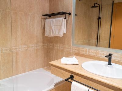 Hell gefliestes Badezimmer mit weißer Badewanne, Waschtisch, rundem Waschbecken und Handtüchern.