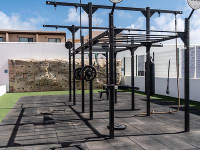 Outdoor-Fitnessbereich mit Kletterwand, Schaukeln, Sprossen und Gummimattenboden unter blauem Himmel.
