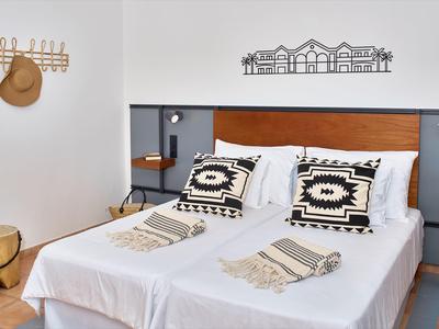 Modernes Schlafzimmer mit zwei Einzelbetten, schwarz-weißen Kissen und Holzdekoration an der Wand.