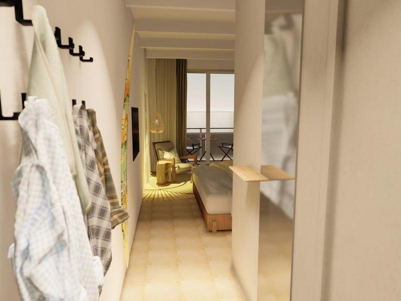 Corridoio stretto con ganci che tengono asciugamani che conduce a una camera d'hotel accogliente con zona salotto e grande finestra.