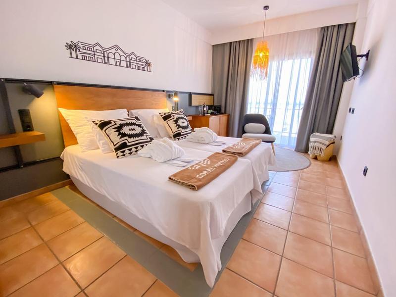 Accogliente camera d'hotel con letto matrimoniale, cuscini decorativi, balcone e arredamento moderno.