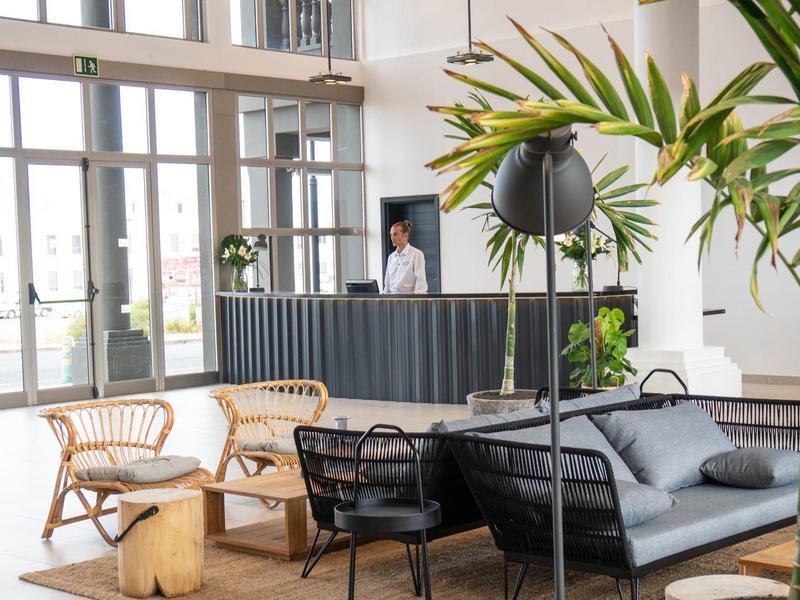 Lobby moderna dell'hotel con area salotto, piante e reception con personale.