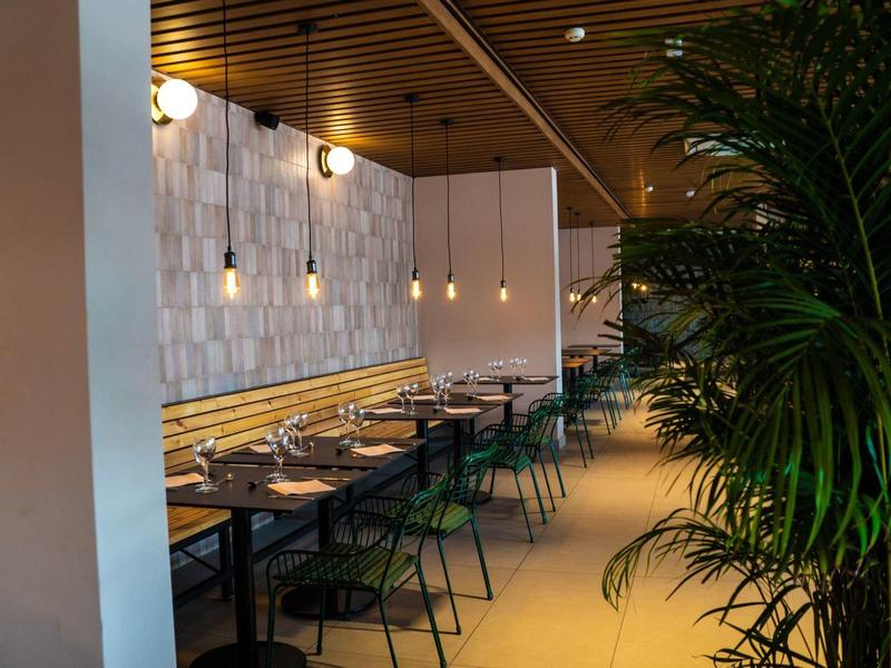 Spazio pranzo moderno con soffitto in legno, luci sospese e sedie verdi lungo i posti a sedere a parete.