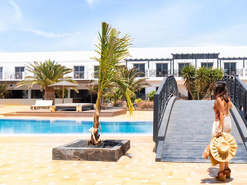 Donna che cammina accanto a una piscina verso un edificio bianco sotto un cielo azzurro limpido