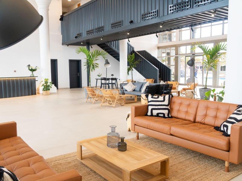 Ampio salone dell'hotel con divani moderni, tavoli in legno, piante e luce naturale.