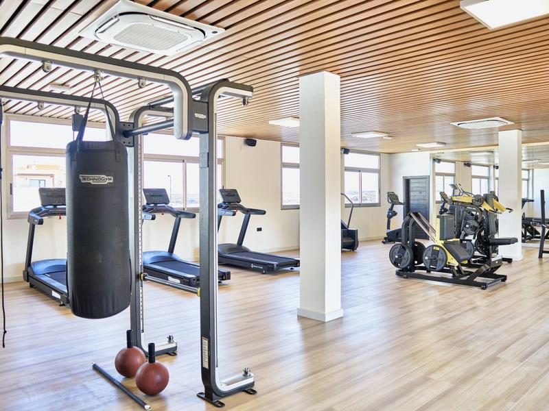 Palestra luminosa dell'hotel con tapis roulant, sacco da boxe e cyclette su pavimento in legno.