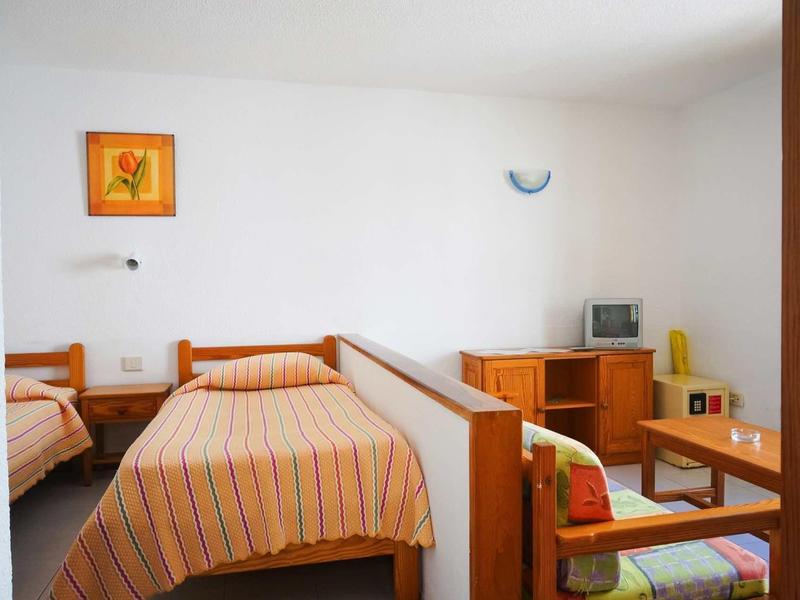 Schlichtes Zimmer mit zwei Einzelbetten, hölzernen Möbeln und einem kleinen Fernseher.