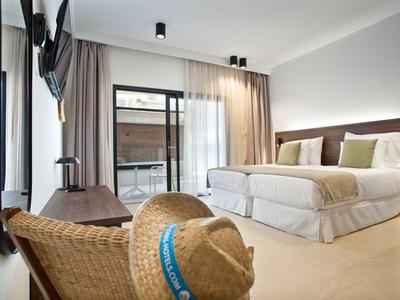Modern hotel room with two single beds, balcony, and chair with a straw hat in the foreground.