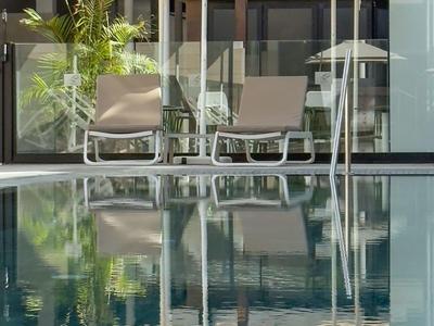 Sun umbrellas and lounge chairs beside a clear pool in front of modern hotel buildings.