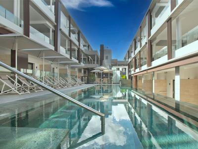 Modern hotel complex with long indoor pool between two building rows under blue sky.