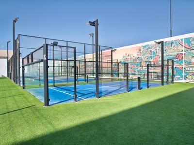 Modern padel court with blue surface, enclosed by tall fences and colorful mural in the background.