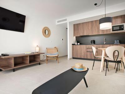 Nowoczesny salon z aneksem kuchennym, sofą, telewizorem i częścią jadalną w neutralnych kolorach.