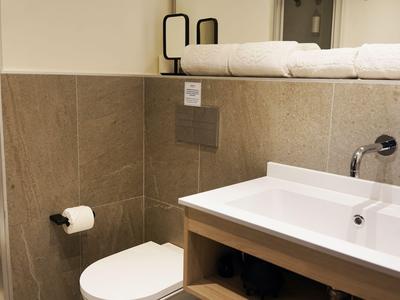 Modern hotel bathroom with toilet, white sink, and beige tones on walls and floor.