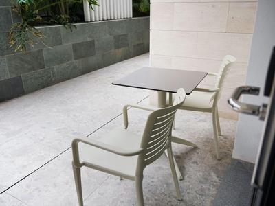Two white chairs and a table on a terrace with light gray flooring next to a wall.
