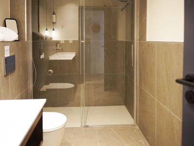Modern hotel bathroom with shower, toilet, and sink in warm beige tones.
