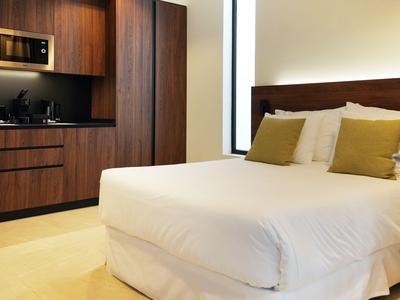 Modern hotel room with double bed, white linens, and an integrated wooden kitchenette.