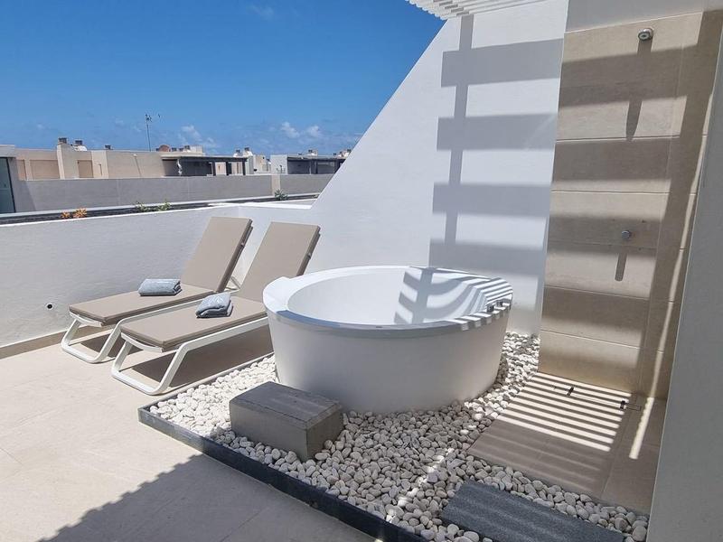 Area esterna moderna con vasca idromassaggio bianca, lettini e cielo azzurro limpido.