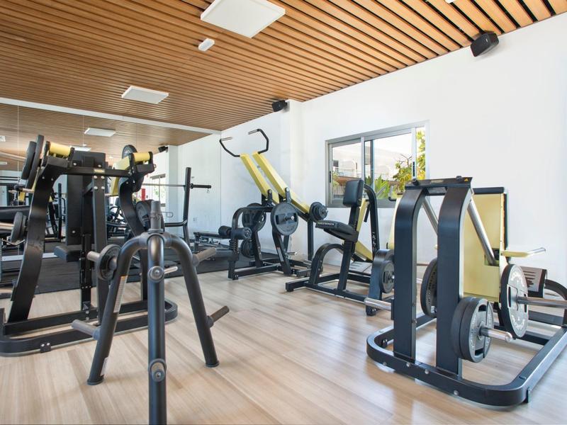Palestra luminosa con varie attrezzature per allenamento di forza e pannelli in legno sul soffitto.