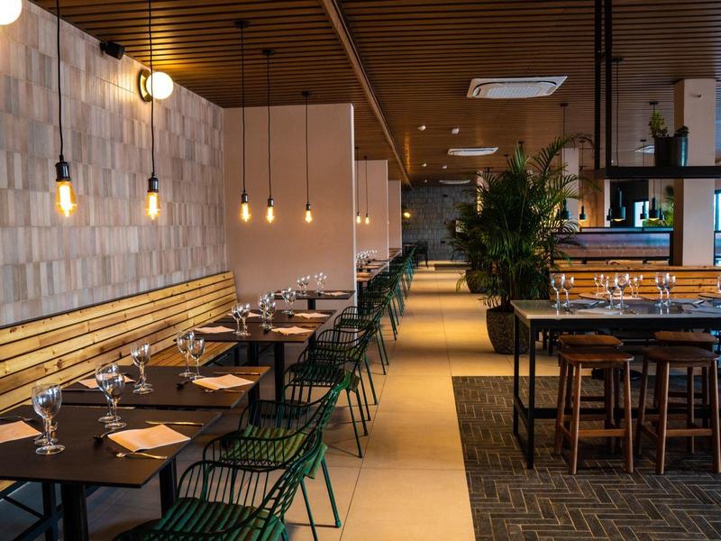 Ristorante moderno con lampadine sospese, tavoli scuri e sedie verdi.