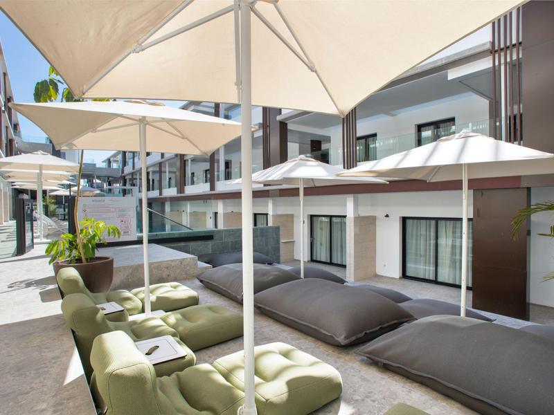 Un'area esterna moderna di un hotel con comodi pouf, sedie e grandi ombrelloni.