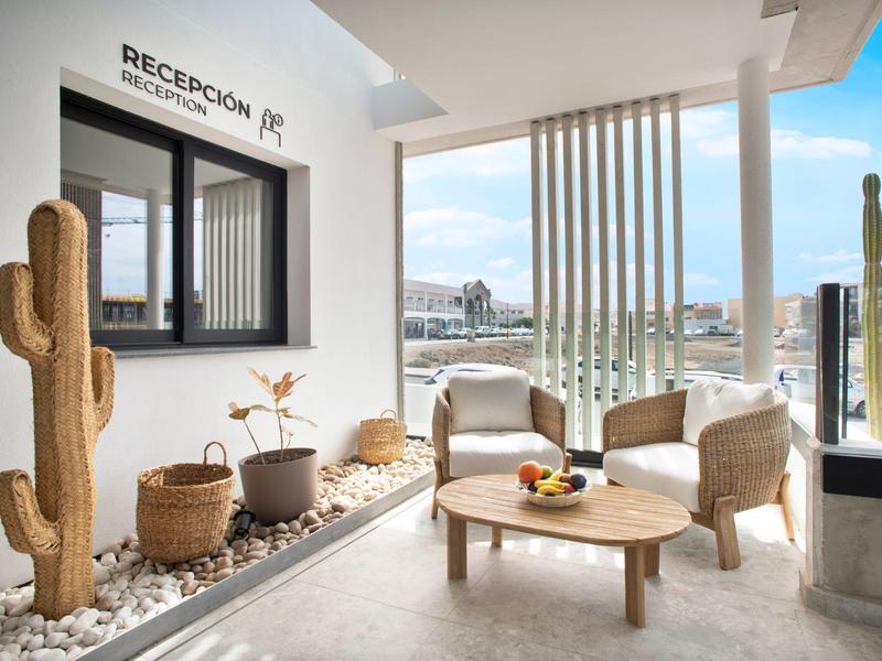 Reception moderna dell'hotel con area salotto, cactus e vista sulla città sullo sfondo.