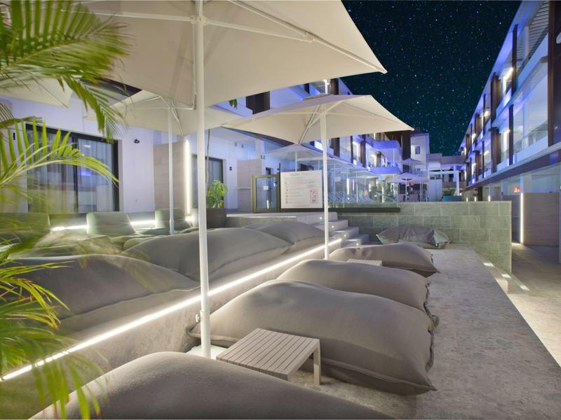 Area esterna moderna con lettini, ombrelloni e illuminazione elegante di notte.