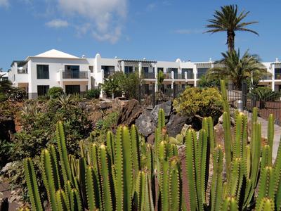 Edifici bianchi dietro un terreno coperto di cactus sotto un cielo azzurro.