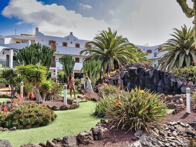 Hotel mit weißen Gebäuden, Palmen und gepflegtem Garten unter blauem Himmel.