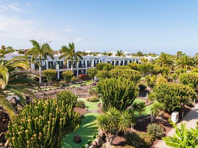 Hôtel avec bâtiment blanc et jardin luxuriant rempli de cactus et de palmiers sous un ciel clair.