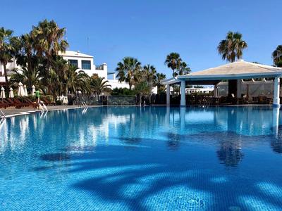 Großer Pool mit klarem Wasser neben Hotelgebäuden und Palmen unter blauem Himmel.
