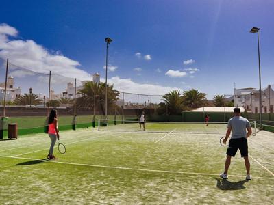 Deux couples jouent au tennis sur un terrain extérieur par temps ensoleillé.