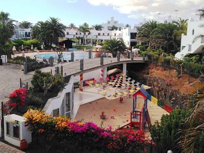 Hotelanlage mit Swimmingpool, Sonnenliegen und blühenden Pflanzen, sonniger Urlaubsort.