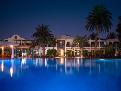 Una piscina dell'hotel illuminata con palme e edifici sullo sfondo di notte.