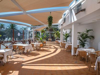 Überdachter Terrassenbereich eines Hotels mit Tischen, Stühlen und Pflanzen bei Tageslicht.
