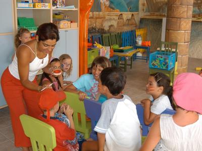 Turista spiega ai bambini in un asilo colorato con sedie e giocattoli.